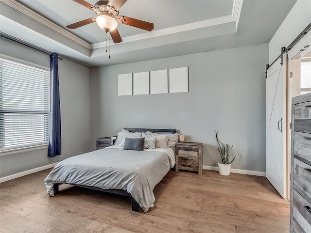 bedroom with a barn door, a raised ceiling, light wood-style flooring, and ornamental molding