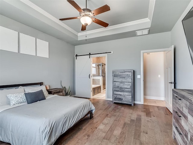 bedroom featuring visible vents, ornamental molding, a tray ceiling, wood finished floors, and a barn door