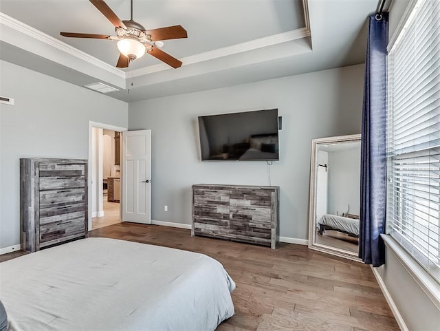 bedroom featuring baseboards, a raised ceiling, wood finished floors, and crown molding