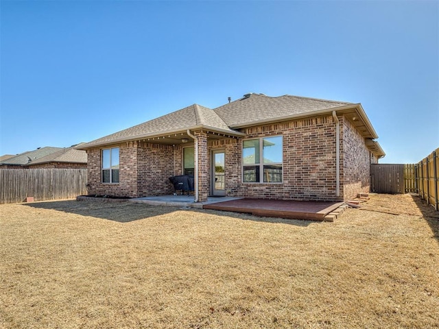 back of house with brick siding, roof with shingles, a yard, a fenced backyard, and a patio area