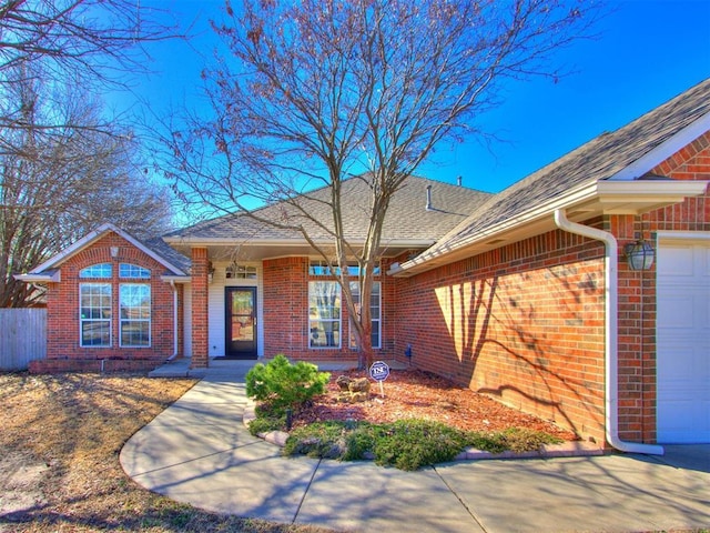 single story home featuring brick siding, an attached garage, roof with shingles, and fence