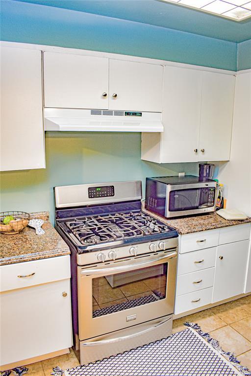 kitchen with under cabinet range hood, stainless steel appliances, light stone countertops, and white cabinetry