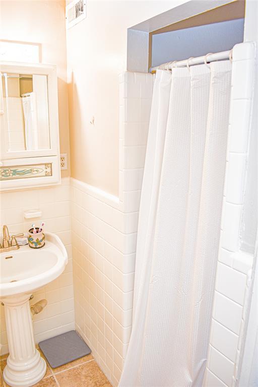 bathroom featuring a shower with curtain, a wainscoted wall, visible vents, tile patterned flooring, and tile walls