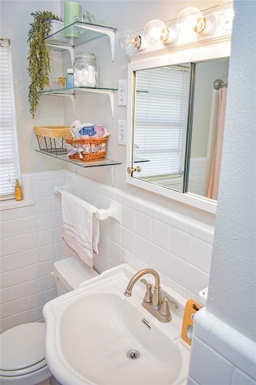 bathroom featuring a sink, toilet, and tile walls