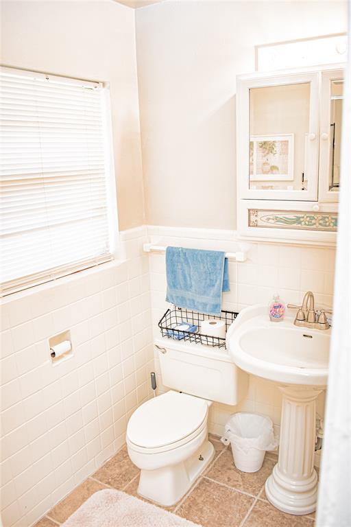 bathroom featuring tile patterned flooring, tile walls, toilet, and a wainscoted wall