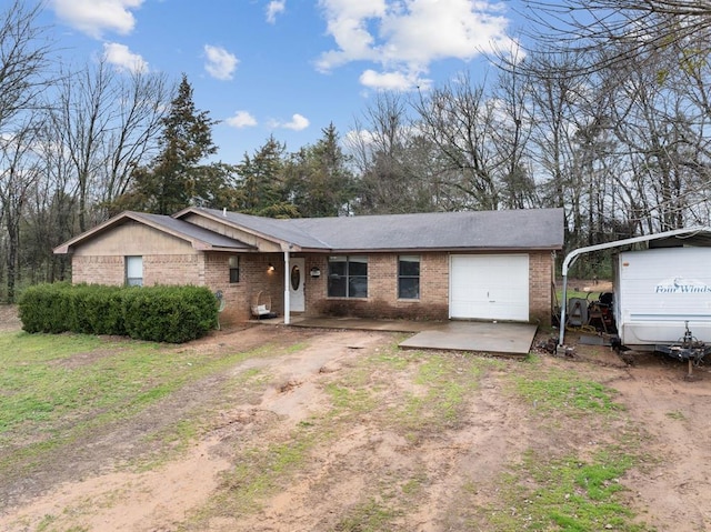 single story home with an attached garage, brick siding, and dirt driveway