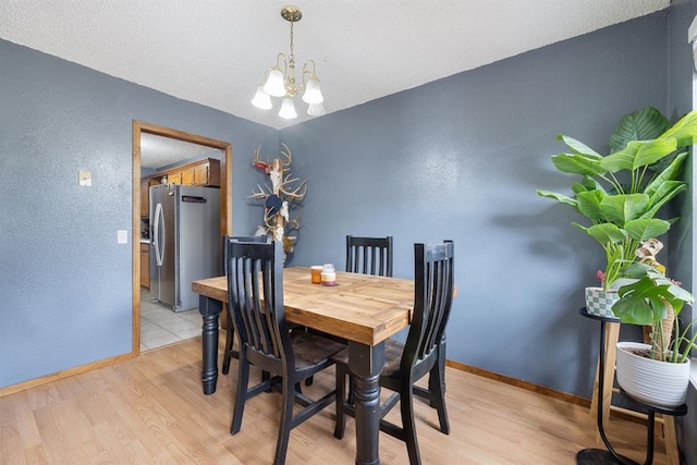 dining room with baseboards, light wood-style floors, an inviting chandelier, and a textured ceiling