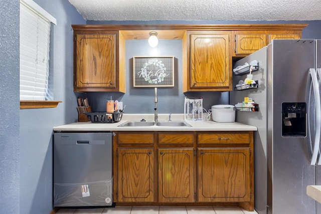 kitchen with light countertops, stainless steel appliances, brown cabinetry, a textured ceiling, and a sink