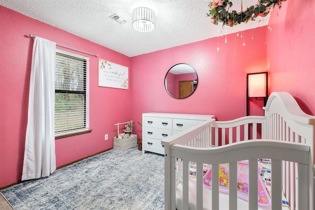 bedroom featuring visible vents, a crib, a textured ceiling, and carpet flooring