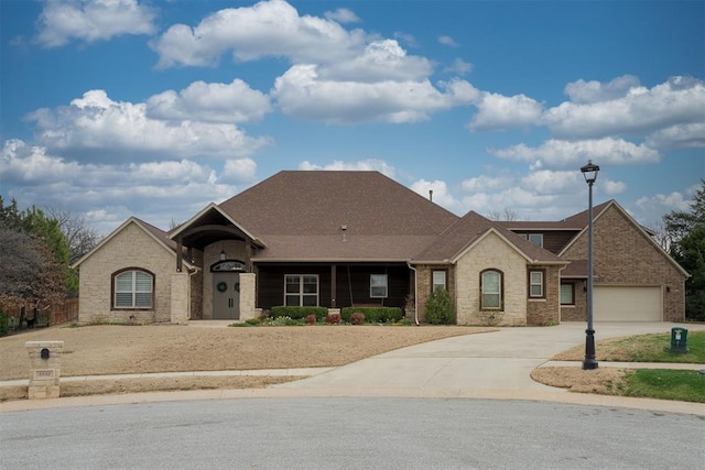 french country inspired facade featuring concrete driveway, brick siding, a garage, and roof with shingles