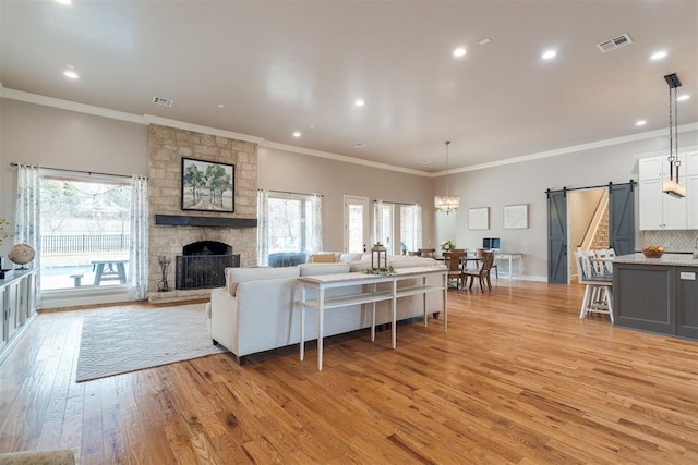 living room featuring visible vents, a stone fireplace, light wood-style floors, a barn door, and a wealth of natural light