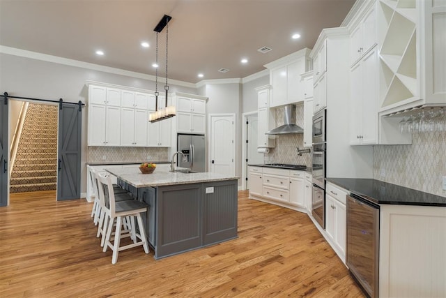 kitchen featuring a sink, a barn door, wine cooler, stainless steel appliances, and wall chimney range hood