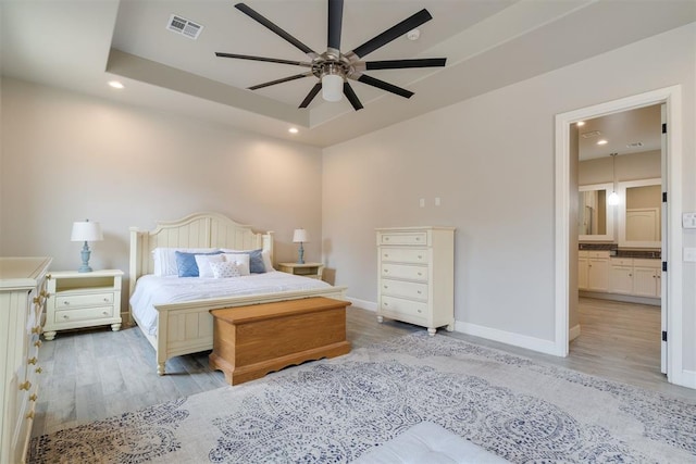 bedroom featuring light wood finished floors, visible vents, and a raised ceiling