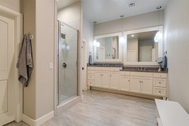 bathroom featuring visible vents, a shower stall, double vanity, wood finished floors, and a sink