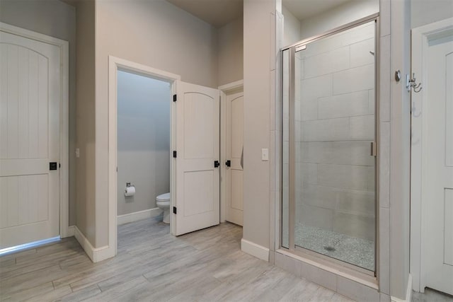 full bath featuring baseboards, toilet, wood finished floors, and a shower stall