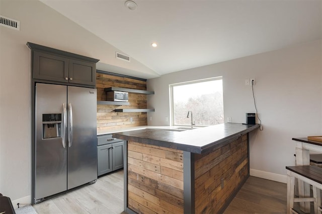 kitchen with light wood finished floors, visible vents, lofted ceiling, stainless steel fridge, and open shelves