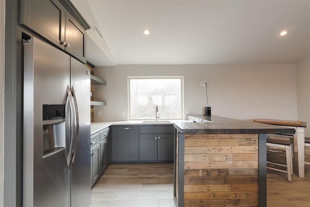 kitchen with open shelves, light wood-style flooring, stainless steel fridge, and a sink