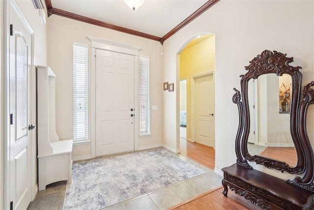 tiled entrance foyer featuring arched walkways, baseboards, and ornamental molding