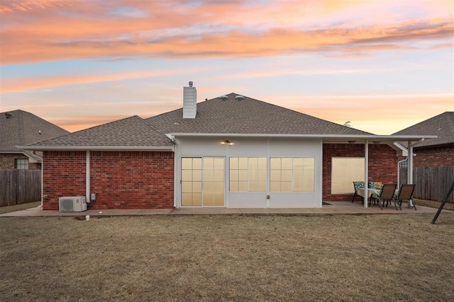 back of property at dusk with brick siding, a lawn, a patio, and fence