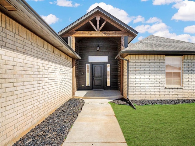 entrance to property featuring brick siding, a lawn, and roof with shingles