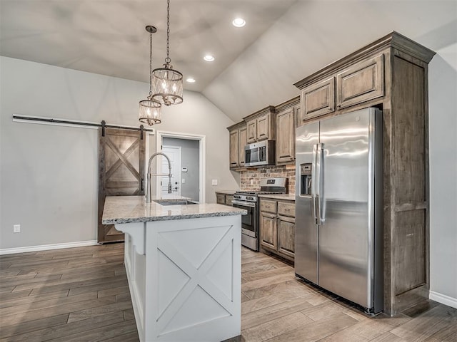 kitchen with a sink, a barn door, wood finished floors, and stainless steel appliances