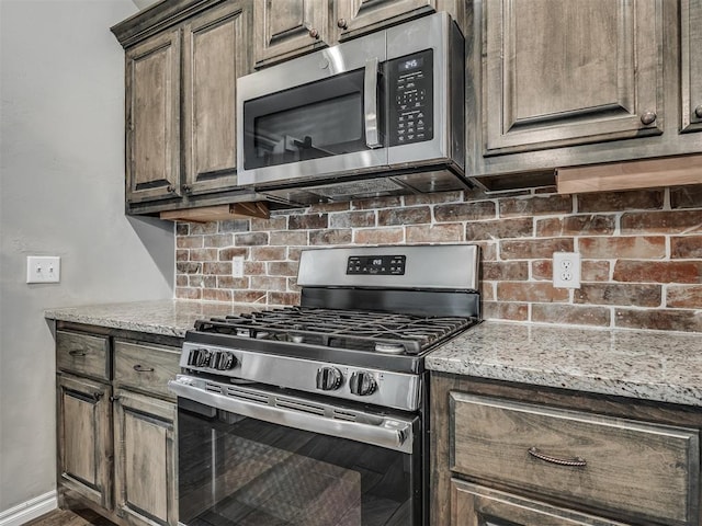 kitchen featuring tasteful backsplash, appliances with stainless steel finishes, baseboards, and light stone counters