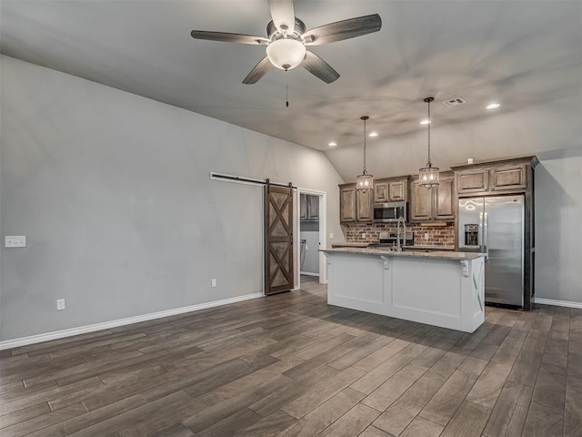 kitchen featuring visible vents, backsplash, dark wood finished floors, a barn door, and stainless steel appliances