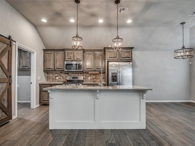 kitchen featuring visible vents, a sink, a barn door, appliances with stainless steel finishes, and a kitchen island with sink