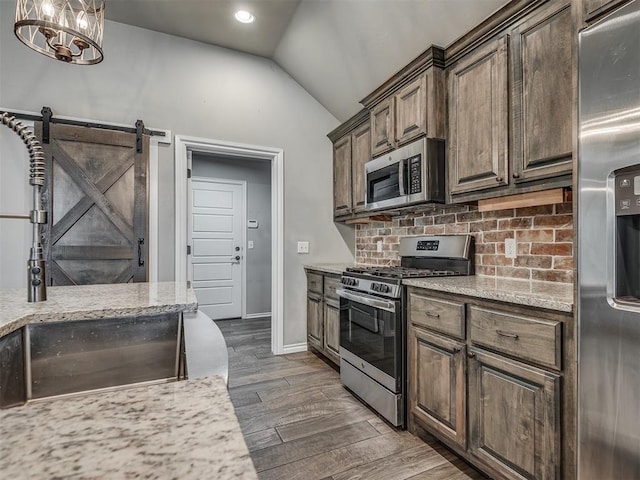 kitchen featuring dark wood finished floors, a sink, decorative backsplash, vaulted ceiling, and stainless steel appliances