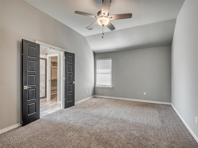 unfurnished bedroom with visible vents, baseboards, vaulted ceiling, a walk in closet, and light colored carpet