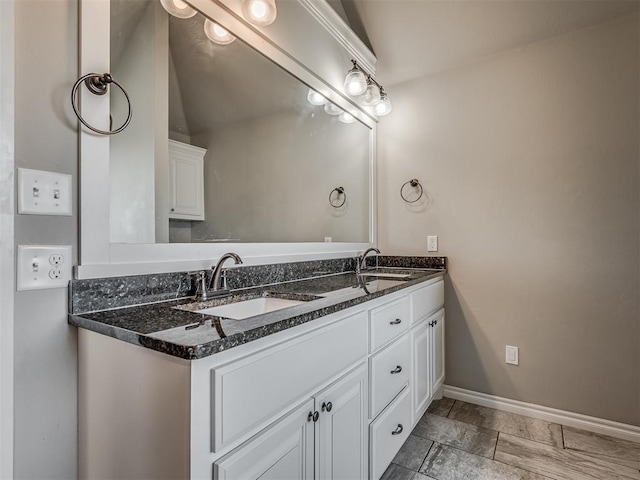 bathroom with double vanity, vaulted ceiling, baseboards, and a sink