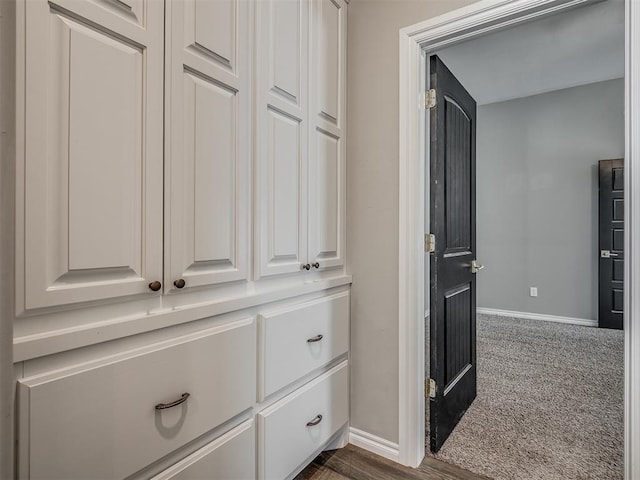 corridor featuring baseboards and dark colored carpet