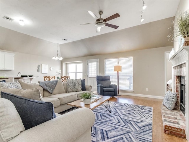 living area featuring visible vents, ceiling fan with notable chandelier, baseboards, a brick fireplace, and vaulted ceiling