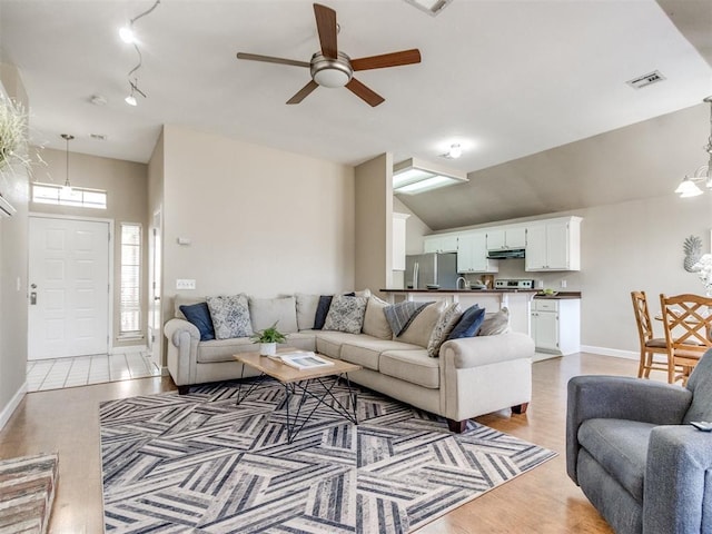 living room featuring visible vents, ceiling fan with notable chandelier, baseboards, and vaulted ceiling