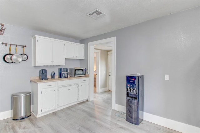 kitchen featuring visible vents, baseboards, light countertops, light wood-type flooring, and white cabinets