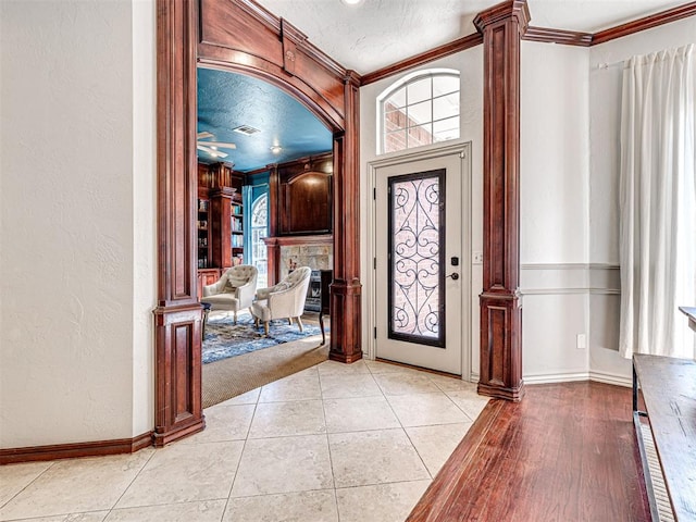 foyer entrance featuring visible vents, a textured ceiling, crown molding, decorative columns, and a textured wall