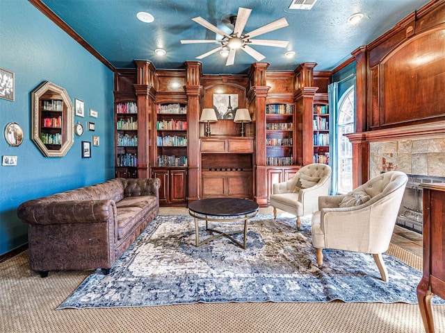 living area with carpet floors, ceiling fan, ornamental molding, a textured ceiling, and a textured wall