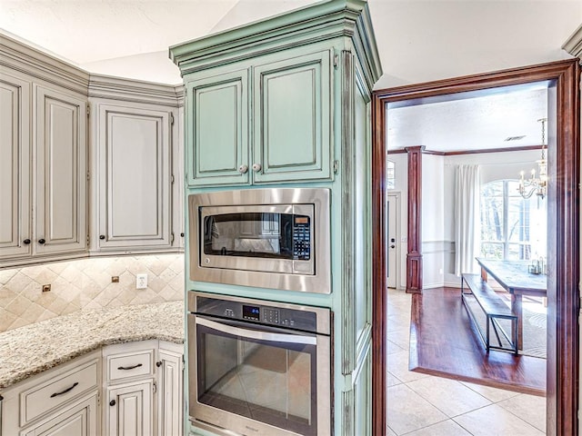 kitchen featuring light stone counters, light tile patterned flooring, appliances with stainless steel finishes, tasteful backsplash, and a chandelier