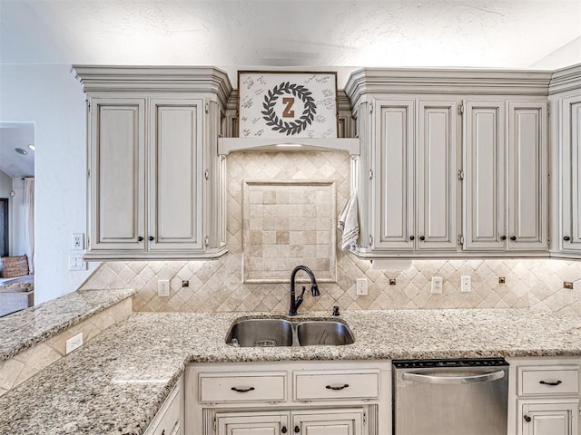 kitchen with a sink, backsplash, light stone countertops, and stainless steel dishwasher