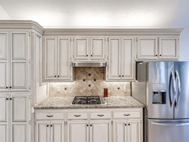 kitchen with light stone countertops, tasteful backsplash, under cabinet range hood, and stainless steel appliances