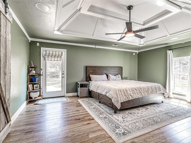 bedroom featuring a barn door, coffered ceiling, ornamental molding, and a textured wall