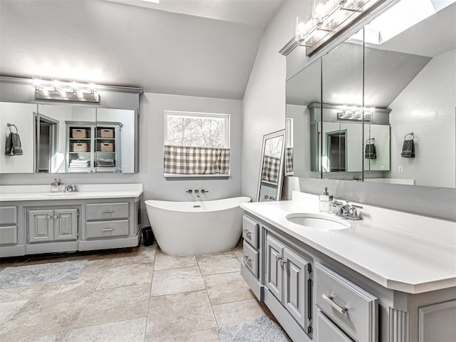 full bath with lofted ceiling with skylight, a freestanding tub, two vanities, and a sink