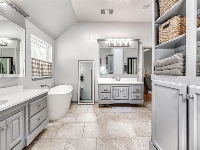 full bathroom featuring visible vents, a freestanding tub, two vanities, a sink, and vaulted ceiling