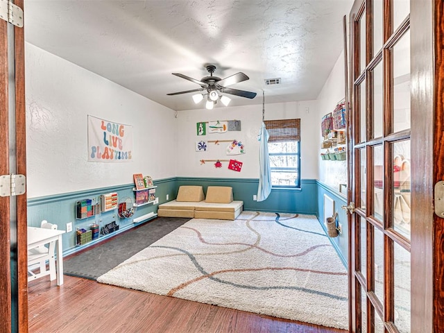 playroom featuring visible vents, wainscoting, ceiling fan, and wood finished floors