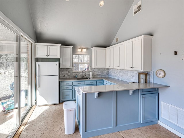 kitchen featuring visible vents, a sink, freestanding refrigerator, a peninsula, and lofted ceiling