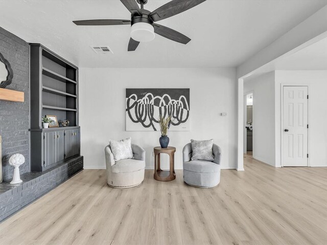 living area featuring visible vents, built in shelves, ceiling fan, and wood finished floors