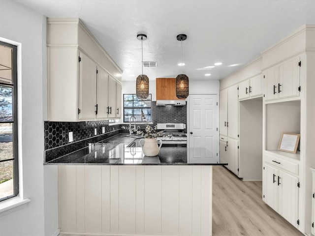 kitchen featuring tasteful backsplash, visible vents, under cabinet range hood, stainless steel range with gas stovetop, and a peninsula