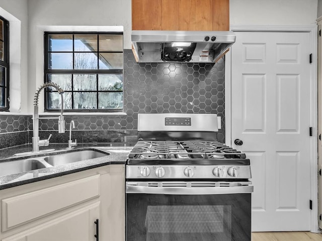 kitchen featuring wall chimney range hood, tasteful backsplash, stainless steel gas stove, and a sink