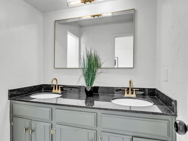 full bathroom featuring double vanity, a textured wall, and a sink