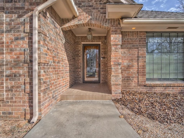 property entrance featuring brick siding and a shingled roof